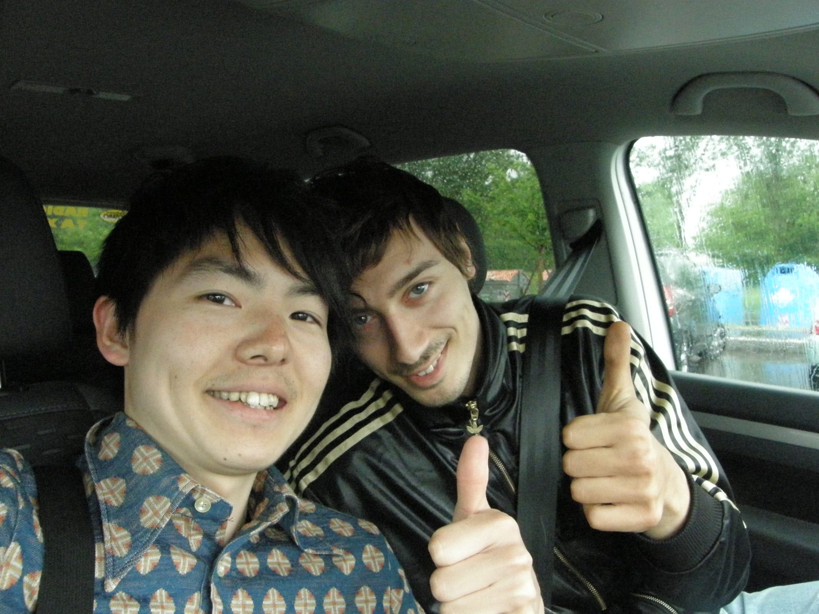 車内で親指を立てる二人の男性。左が本人