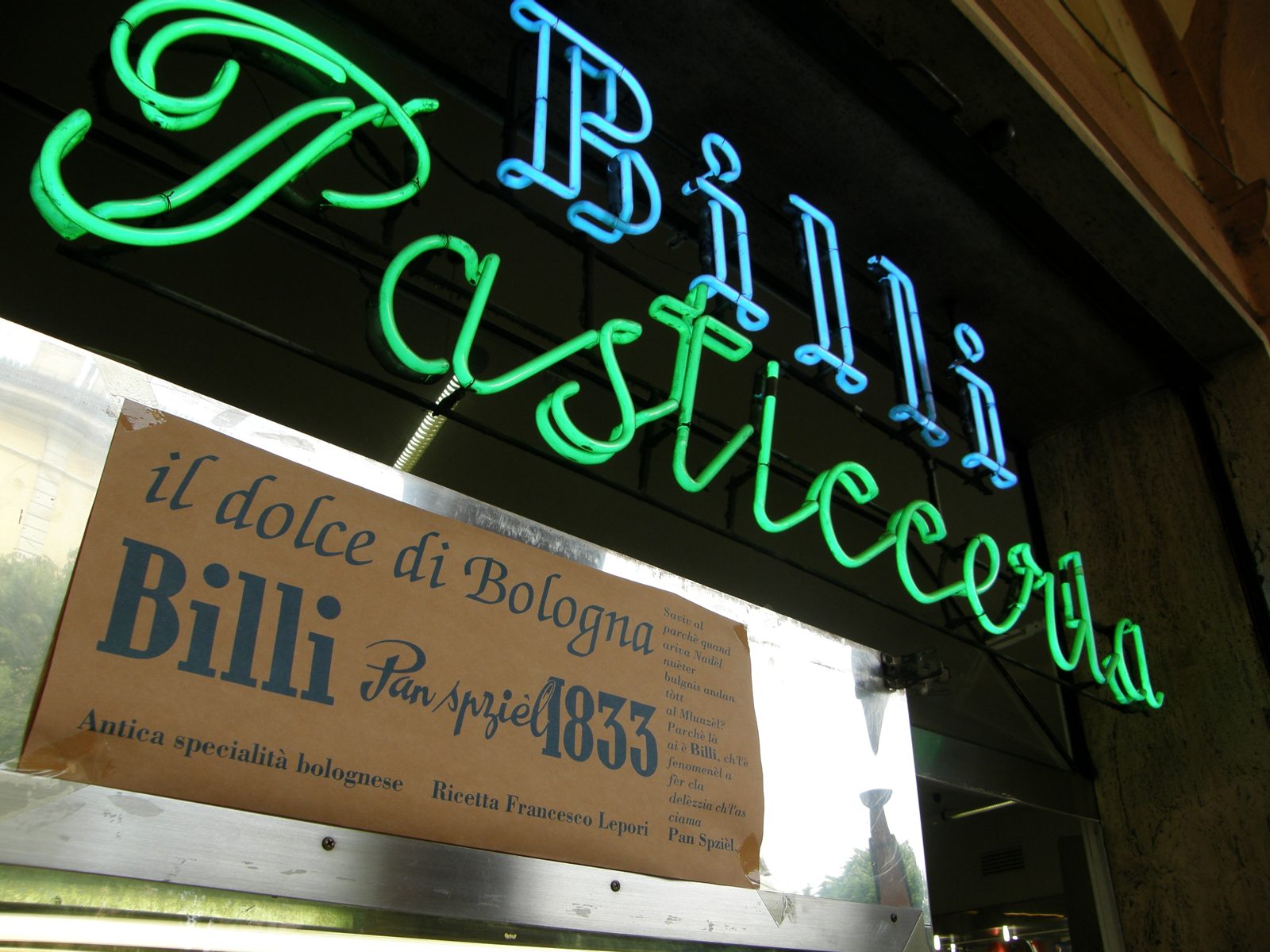 緑と青のネオンで Billi Pasticceria と書かれた看板と、その下の古い木の看板