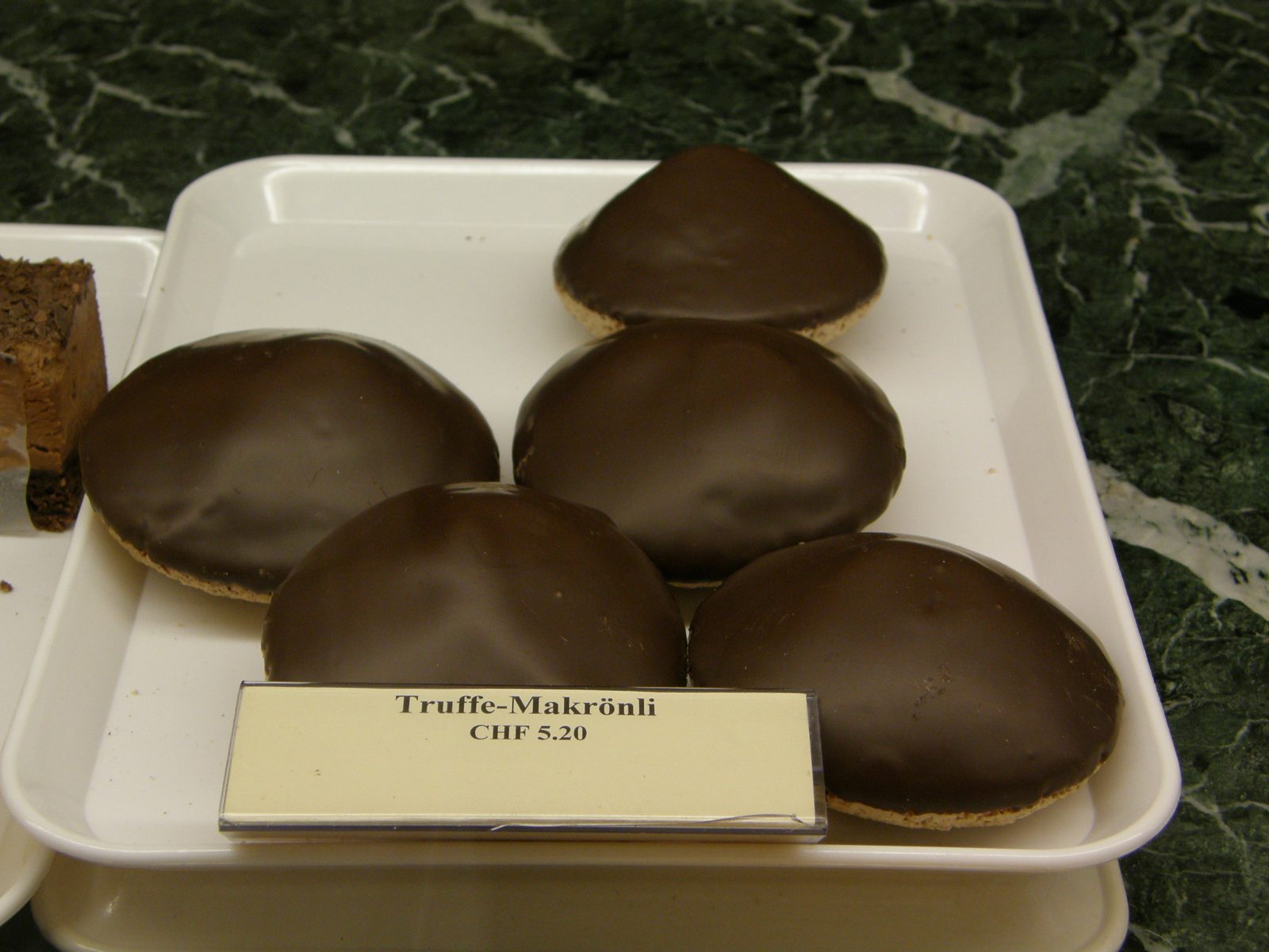 チョコレートで覆われた円錐形の菓子が皿に四つ。札に Truffe-Makrönli CHF 5.20