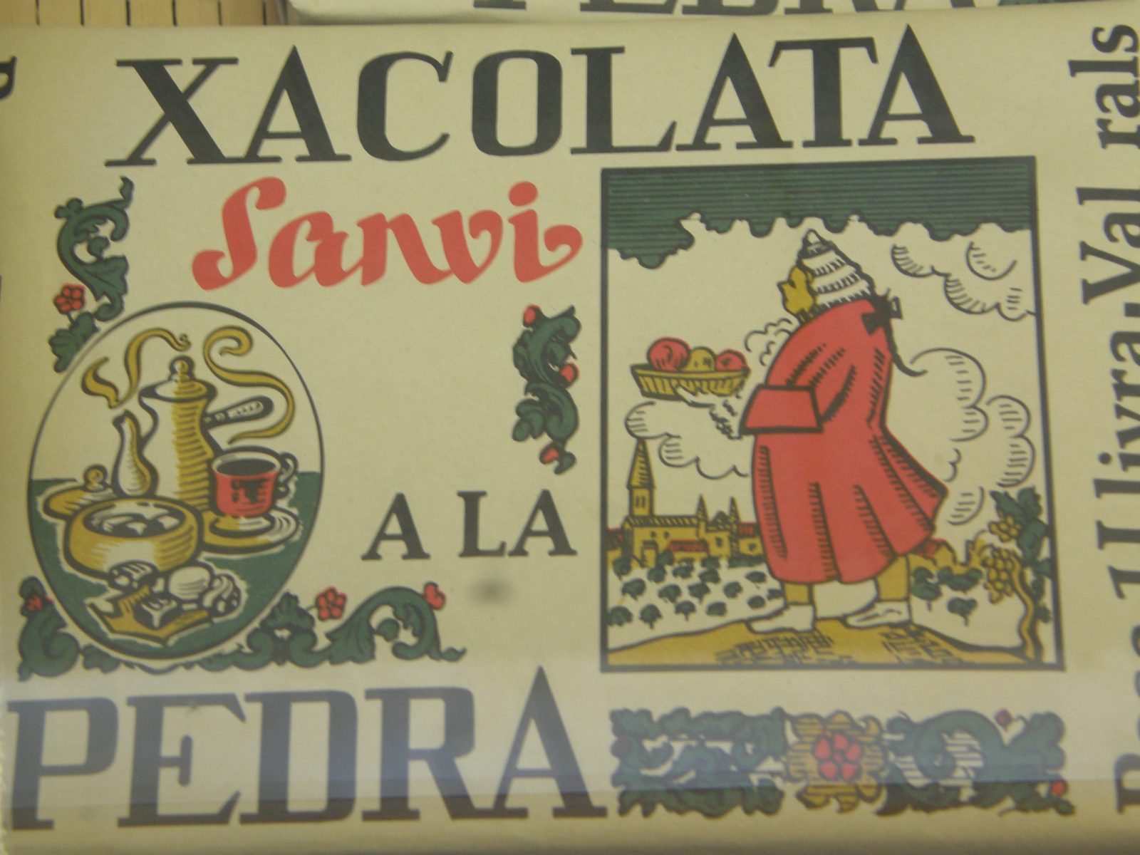 クリーム色の包み紙に、大きく XACOLATA と Sanvi、A LA PEDRA の文字。赤い服の人物と器の絵