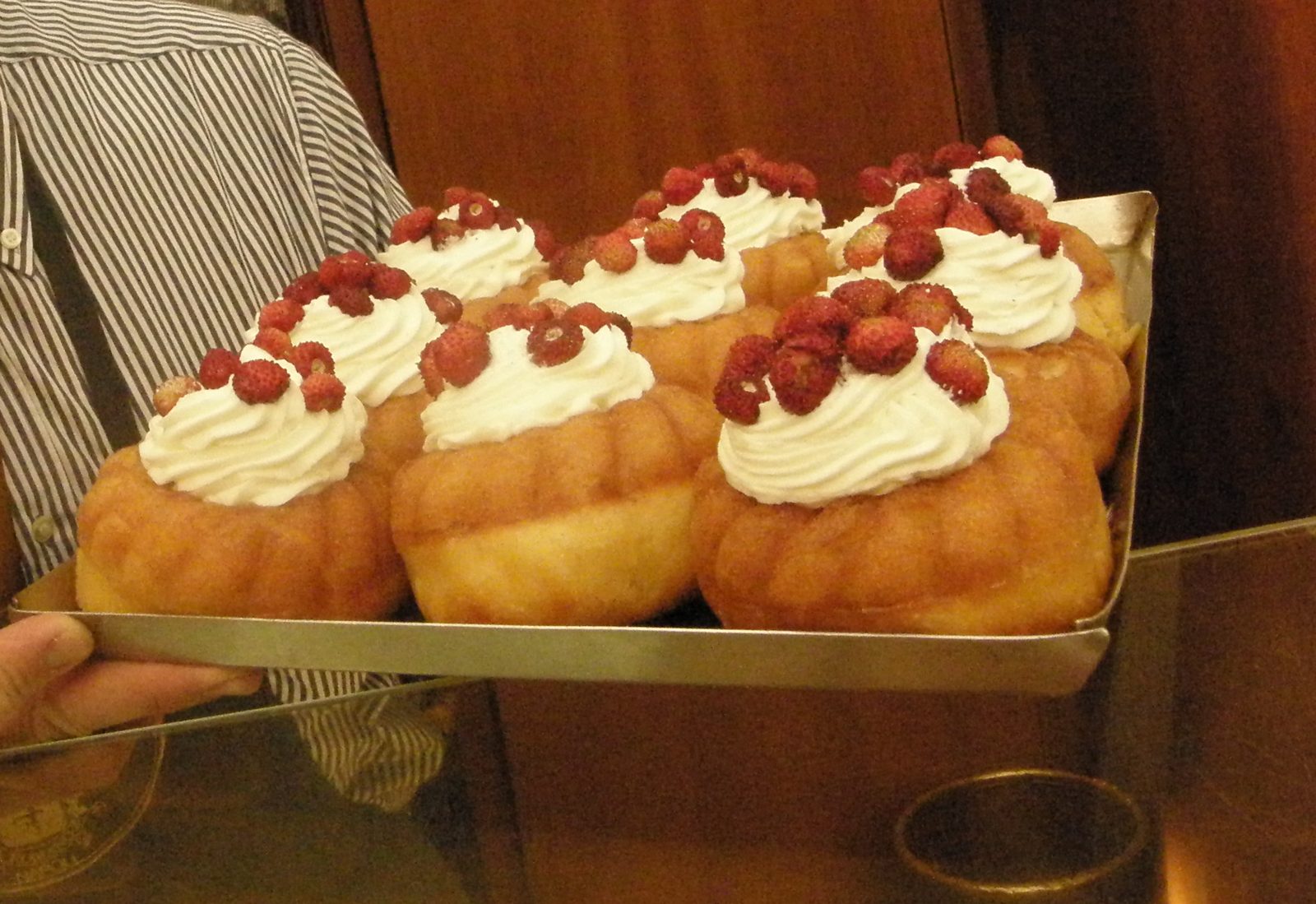 金属のトレイに、白い生クリームと赤い小さないちごをのせたババが並ぶ