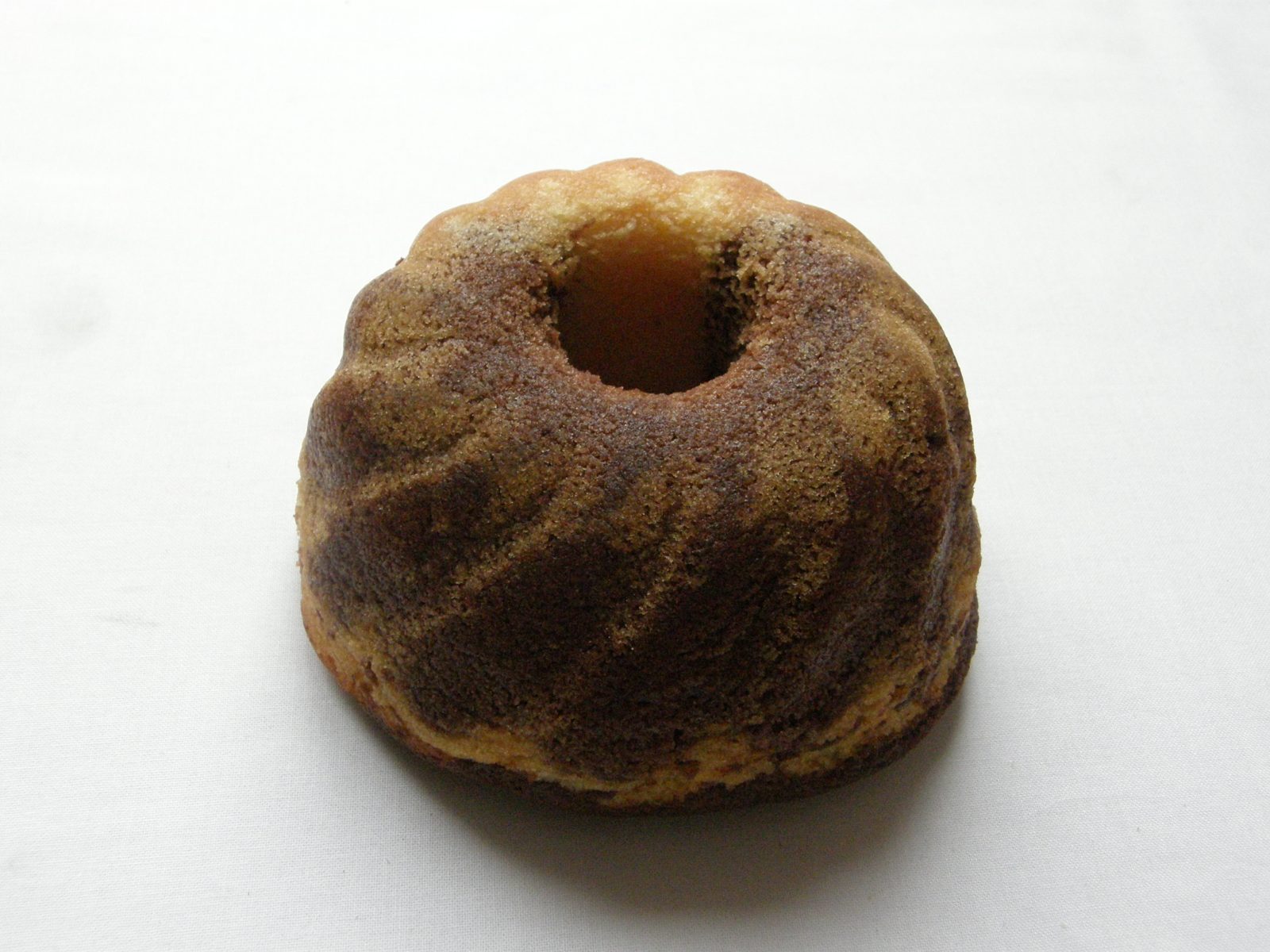 白い布の上に、真ん中に穴のあいた小さな山形の焼き菓子。表面に溝があり、明るい色と茶色の生地が渦のように混ざっている