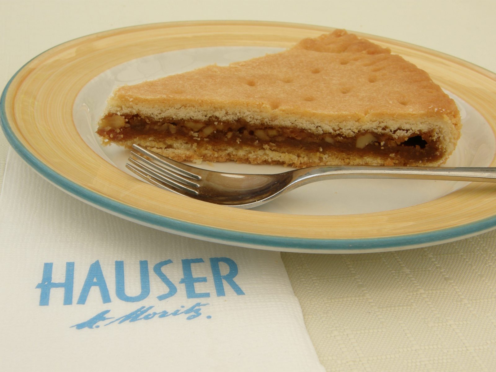 HAUSER St. Moritz と書かれた皿に、三角に切った焼き菓子とフォーク。切り口に茶色いくるみの詰め物