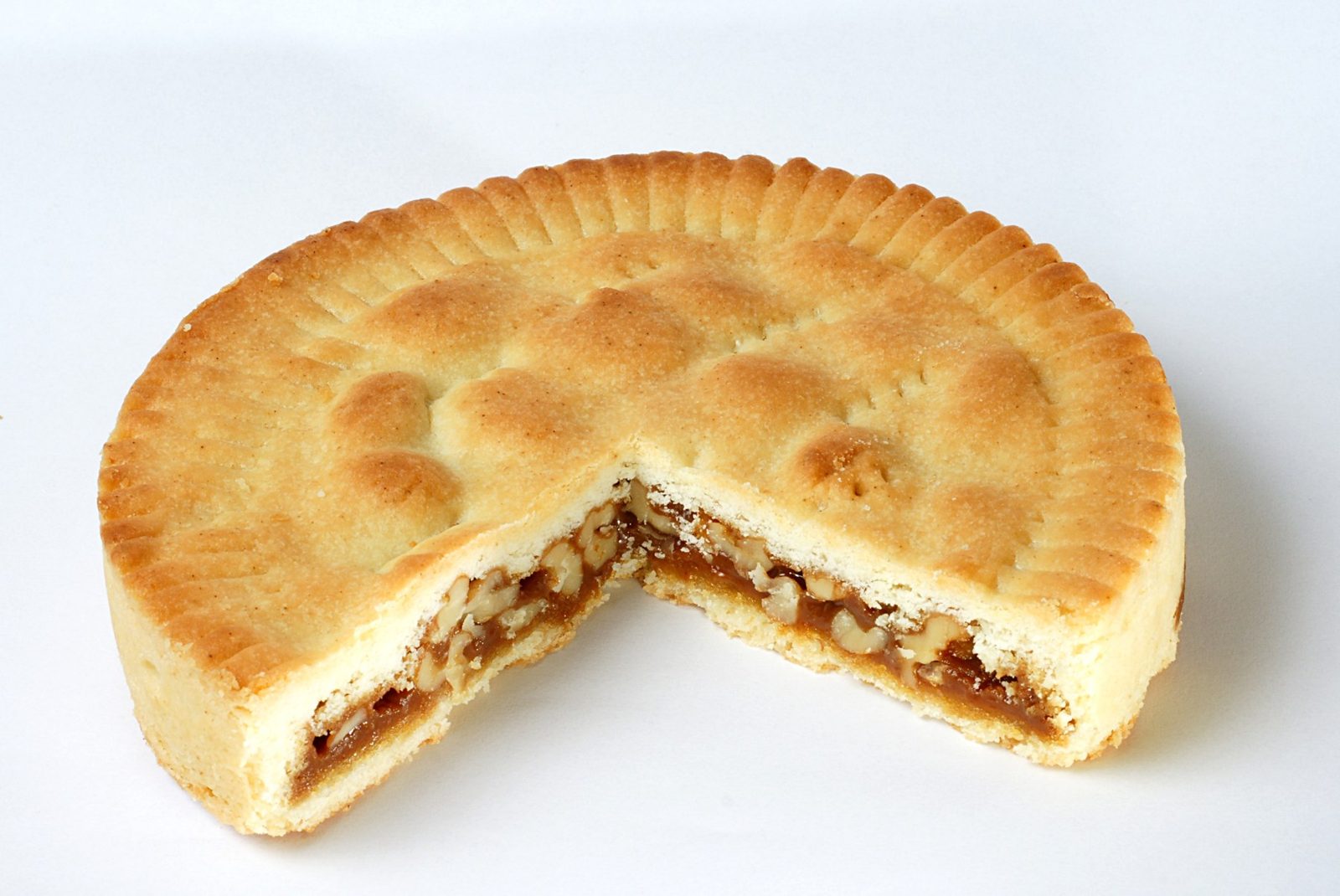 白い背景に、丸く平たい焼き菓子。一切れ分が切り取られ、断面に茶色いキャラメルとくるみの層