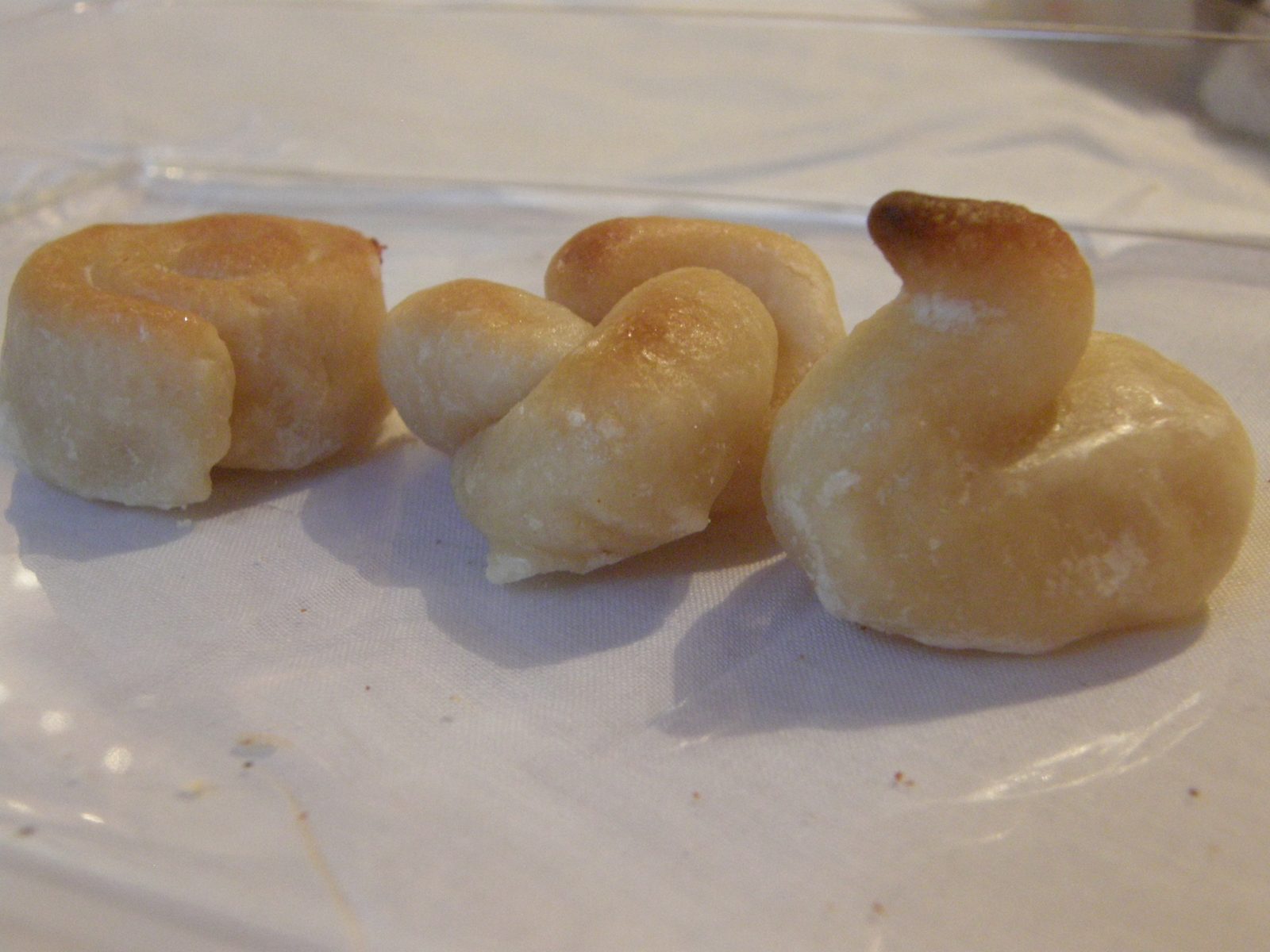 白い布の上に、淡いクリーム色の小さな焼き菓子が三つ。渦巻き形、結び目形、鳥の形で、上の先だけ茶色く焼けている