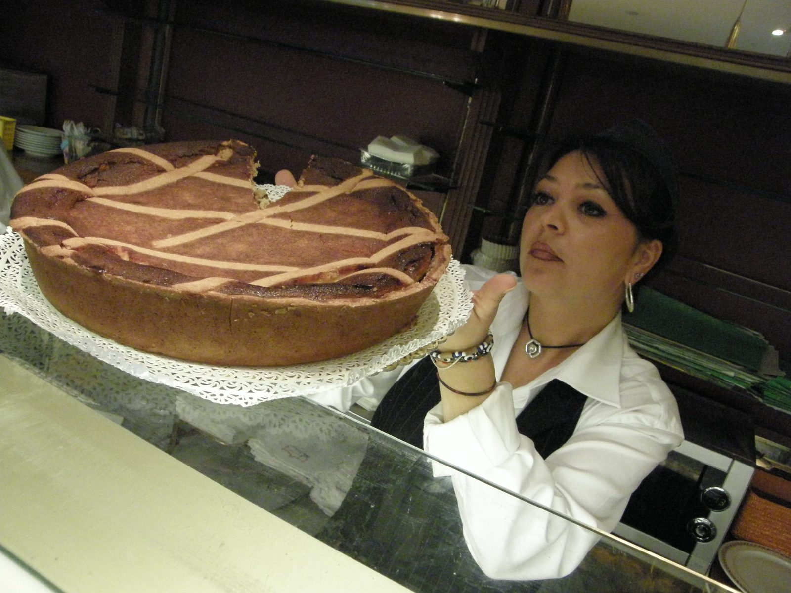 ショーケースの向こうで、店の女性がレースの紙にのった大きな丸いタルトを持ち上げている