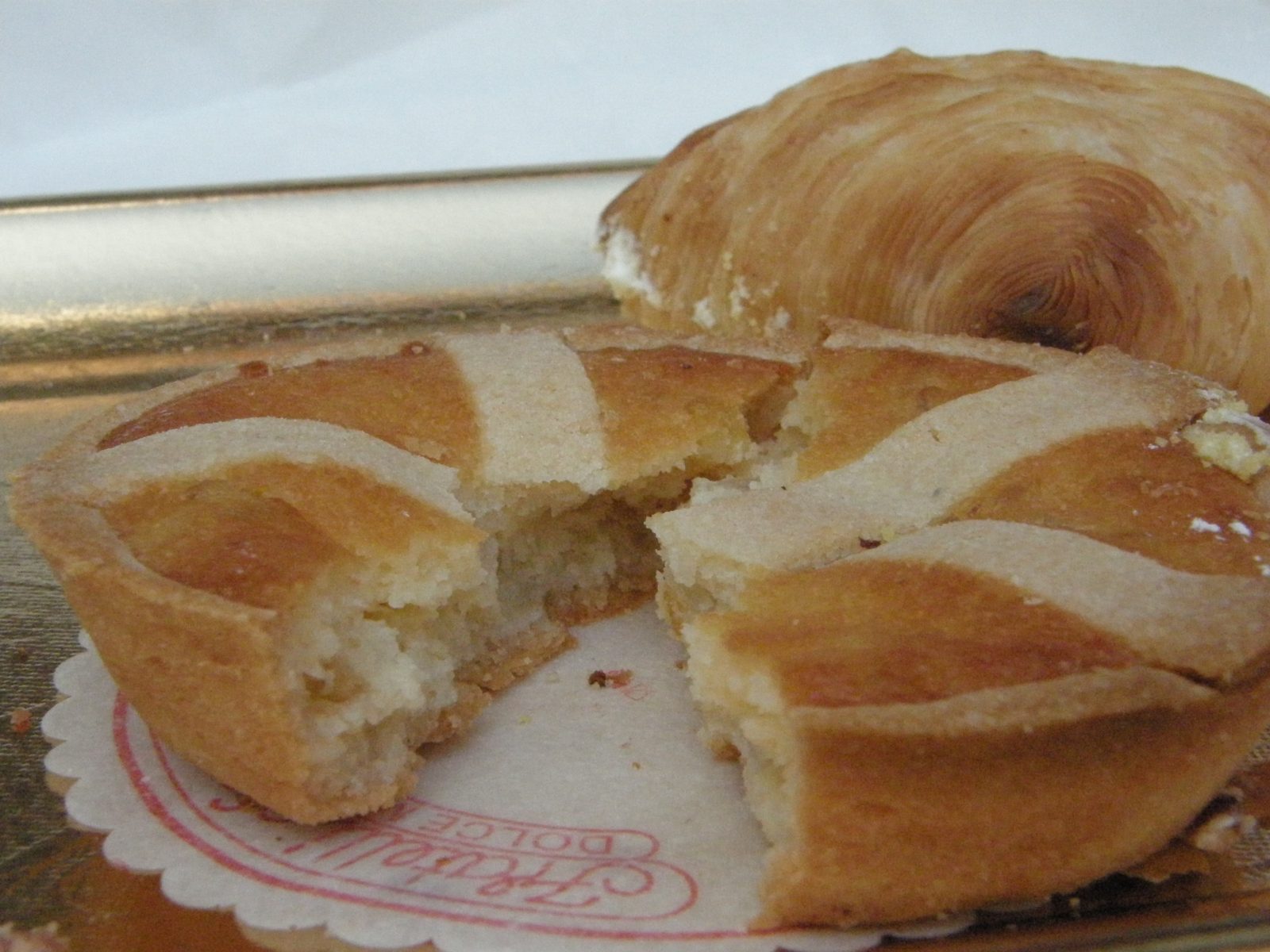 割った小さなタルトの断面。黄色っぽいしっとりした詰め物がのぞく。奥に貝殻形の焼き菓子