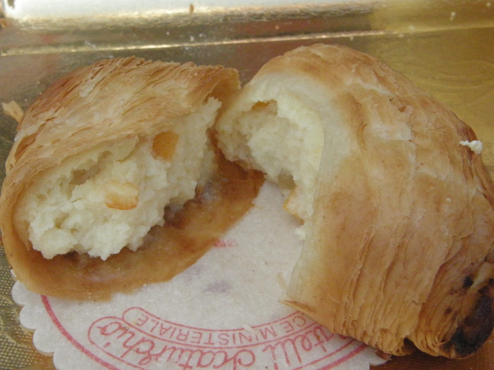 割った貝殻形の焼き菓子の断面。外側に薄い層が重なり、内側に白いクリームとオレンジ色の粒