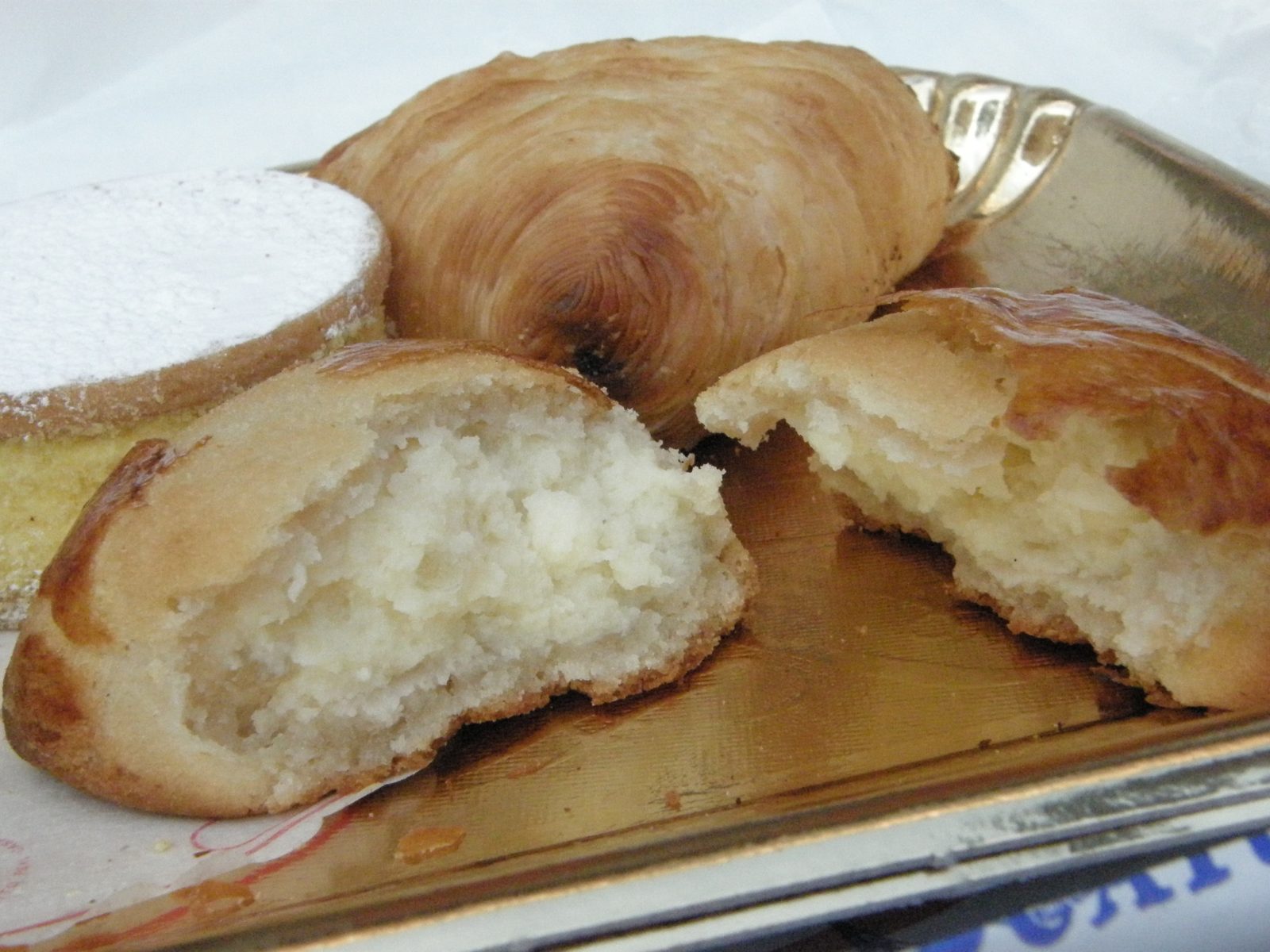 割った丸い焼き菓子の断面。なめらかな生地の中に白いクリーム。奥に貝殻形の菓子と、粉砂糖をかけた丸い菓子