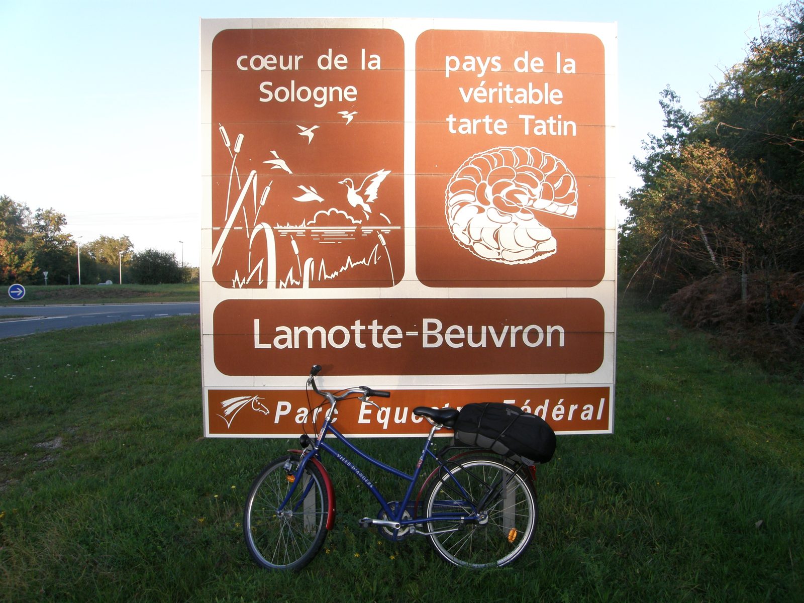道路脇の茶色い標識に Lamotte-Beuvron の地名と、本物のタルト・タタンの地であることを示す文字。手前に自転車