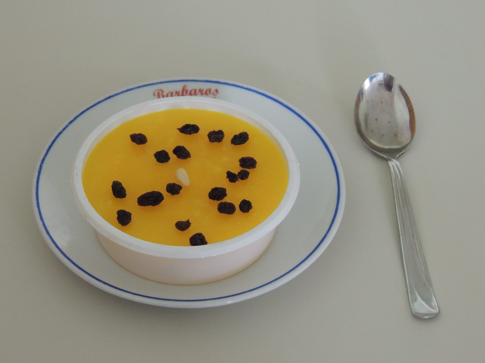 白い器に入った黄色いなめらかな甘い粥。上にレーズン。皿に店名「Barbaros」