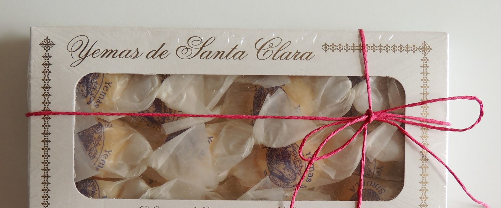 白い箱に筆記体で Yemas de Santa Clara。透明な窓の中に、紙で包んだ小さな玉が並び、赤い紐で結んである